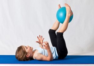 Young girl practicing balance exercises with a blue yoga ball indoors on a mat.